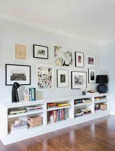 a white book shelf filled with books on top of a hard wood floor next to a wall covered in framed pictures