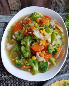 a white bowl filled with vegetable soup next to a piece of bread on top of a table