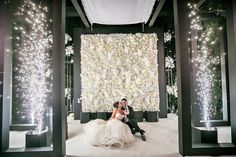 a bride and groom are sitting in front of a floral wall at their wedding reception