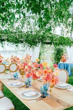 a wooden table topped with plates and vases filled with flowers next to a lush green field