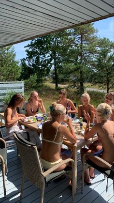 a group of people sitting around a table on a deck eating food and drinking wine