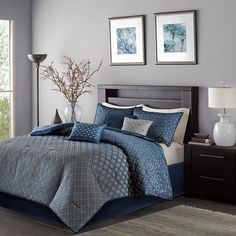 a bed with blue comforter and pillows in a room next to two pictures on the wall