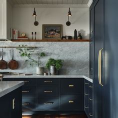 a kitchen with blue cabinets and marble counter tops, brass pulls on the doors, hanging potted plants