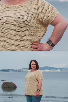 a woman standing on top of a beach next to the ocean and wearing a knitted sweater