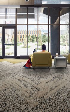 a person sitting on a couch in a room with large windows and a rug covering the floor