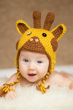 a baby wearing a crocheted giraffe hat on top of white fur