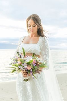 a woman standing on top of a beach holding a bouquet