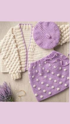 two knitted sweaters and one crochet hat are on the floor next to lavender flowers