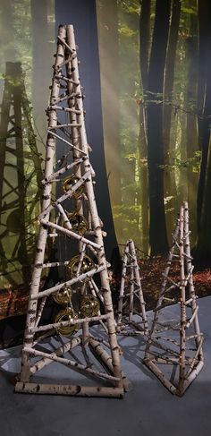 three small trees made out of branches in front of a forest wallpapered with sunlight