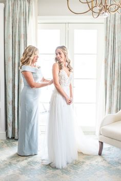 two women standing next to each other in front of a chandelier and window