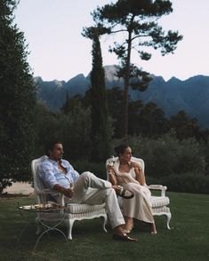 two people sitting on lawn chairs in the grass with mountains in the backgroud