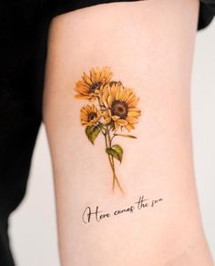 a sunflower tattoo with the words here comes the sun written in cursive font