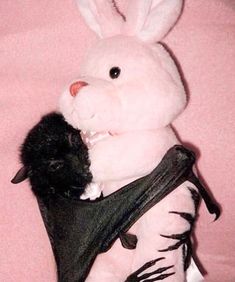 a stuffed rabbit is holding a black cat in it's lap, while sitting on a pink blanket