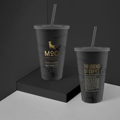 two coffee cups sitting on top of a black table next to each other with straws in them