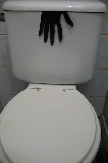 a white toilet with black gloves on the lid and hand prints on the tank cover