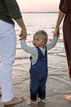 a little boy holding the hand of his mother and father on the beach at sunset