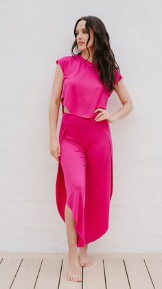 a woman standing in front of a white wall wearing a pink top and matching pants