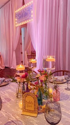 a table with flowers and candles on it in front of a pink curtained room