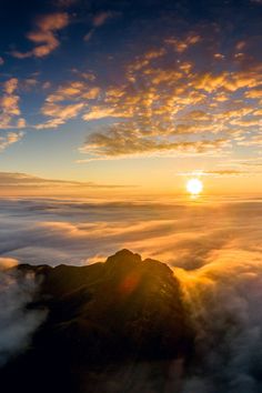 the sun is setting on top of a mountain with clouds in the foreground and below