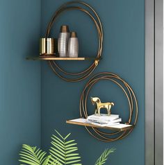 two metal shelves with gold decorations on them against a teal wall and green plant