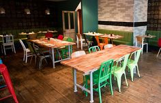 the interior of a restaurant with green and red chairs, wood tables and white walls