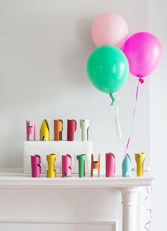 a birthday cake and balloons on a mantle with the words happy birthday spelled in multicolored letters