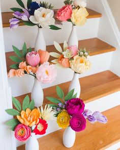 three white vases with colorful flowers in them sitting on the steps leading up to a set of stairs