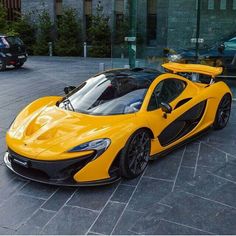 a yellow and black sports car parked in front of a glass building with cars behind it