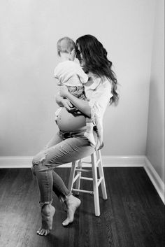 a woman sitting on top of a stool holding a baby in her arms and looking at the wall