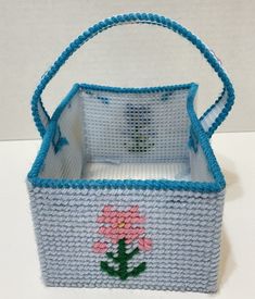 a blue basket with a pink flower on the front and bottom, sitting on a white surface