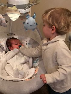 two young children standing next to each other near a baby in a crib with stuffed animals