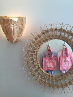 two bags are hanging on the wall in front of a round mirror that is next to a wicker basket