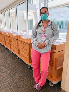 a woman in pink pants and a face mask standing next to some drawers with medical supplies on them