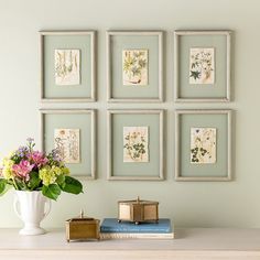 a vase with some flowers on top of a table next to books and pictures hanging on the wall