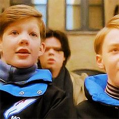 two young boys are standing in front of some other men and one is wearing a blue jacket