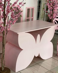 a pink and white butterfly bench next to a tree in a room with tile flooring