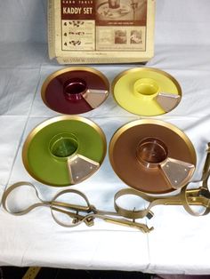 four different colored plates and scissors on a white tablecloth with an old box in the background