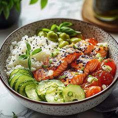 a bowl filled with salmon, cucumbers and rice on top of a table