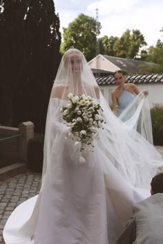 the bride is walking down the aisle with her veil over her head and flowers in her hand