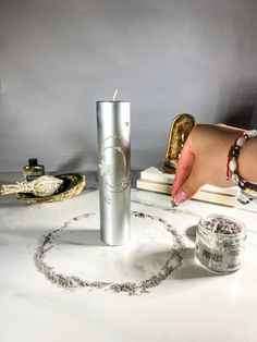 a woman's hand reaching for a candle on a table with other items around it