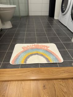 a bathroom with a rainbow rug on the floor and washer in the background, next to a toilet