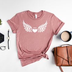 Angel Wings T-shirt, Angel Wings Shirt, Angel Tee, Angel Mama Shirt, Gifts for Mom, Women Graphic Tee, Mothers Day Gift How to Order?  1-Choose your t-shirt color, 2- Choose your size, 3- Select the quantity, 4- Click Add to Cart.  Production and shipping: * 100% airlume combed and ring-spun cotton, 32 singles 4.2 oz. * Solid colors are %100 cotton * Heathers are %52 cotton %48 polyester * Athletic Heather is combed and ring-spun cotton, 10% polyester * Seamless collar * Heat transfer label * Pr Relaxed Fit Tops With Heart Graphic For Gifts, Crew Neck T-shirt With Heart Graphic As Gift, Crew Neck Shirt With Heart Graphic For Gift, Crew Neck Shirt With Heart Graphic As Gift, Angel Mama, Handmade Angels, Women Graphic, Mama Shirt, Color 2