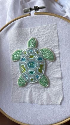 a close up of a cross stitch pattern on a white piece of cloth with a green turtle in the center