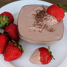 some strawberries are on a white plate near a bowl of chocolate pudding and three strawberries