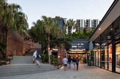 people are walking down the stairs in front of shops and palm trees at dusk or dawn