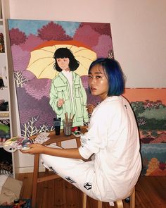 a woman with blue hair sitting in front of a painting holding an umbrella over her head