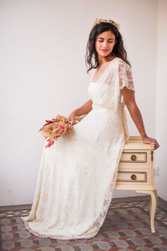 a woman in a white dress is sitting on a small table holding a flower bouquet