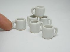 five white coffee mugs sitting next to each other on top of a table with a finger pointing at them