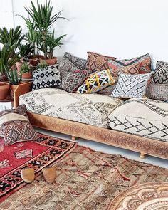 a couch covered in lots of pillows next to potted plants