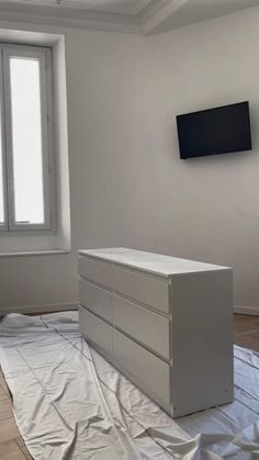 a white dresser sitting on top of a hard wood floor next to a flat screen tv